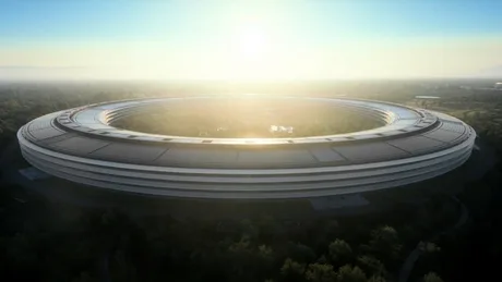 Vedere panoramică a sediului Apple în lumina dimineții, cu soarele răsărind în fundal.
