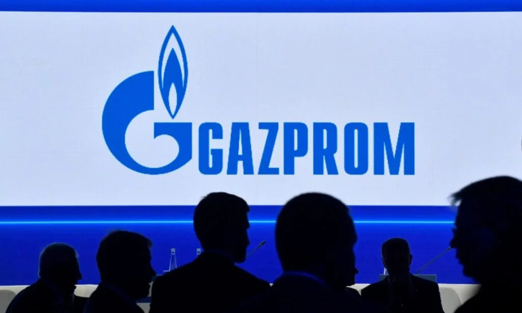 Logo Gazprom pe fundal albastru, cu siluete de oameni în față.