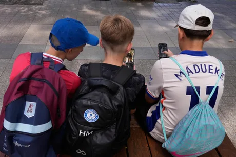 Tineri folosind telefoane mobile pe o bancă în parc.