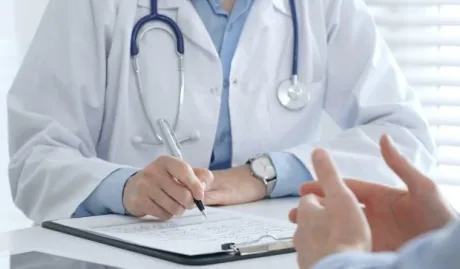 Consult medical între un doctor și un pacient, cu documente pe masă.