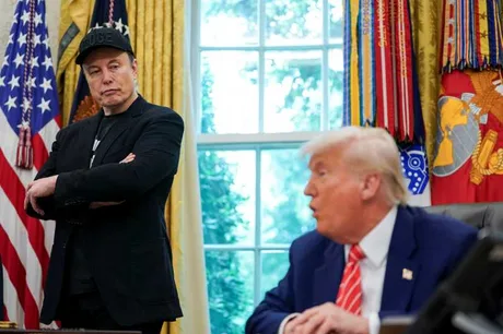 Elon Musk și Donald Trump discutând în Biroul Oval, cu steaguri în fundal.