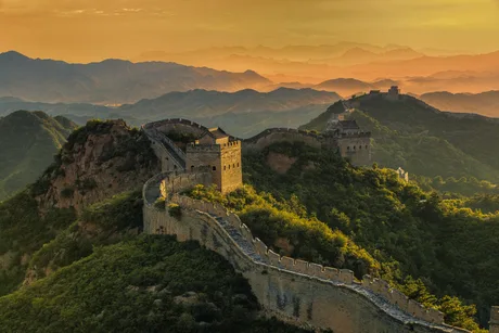 Marele Zid Chinezesc în lumina apusului, cu peisaje montane în fundal.