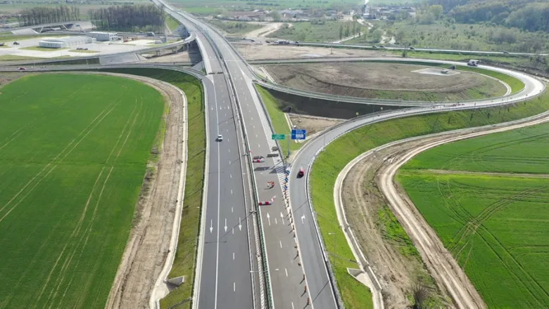 Vedere aeriană a unei autostrăzi în construcție, cu câmpuri verzi în jur.