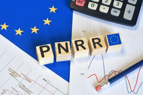 Blocuri de lemn cu litere PNRR pe un fundal european și grafice financiare.