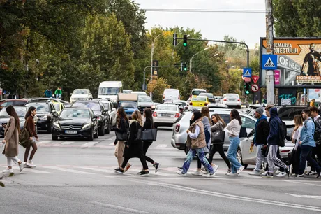 Trecere de pietoni aglomerată într-un oraș, cu oameni și mașini în mișcare.