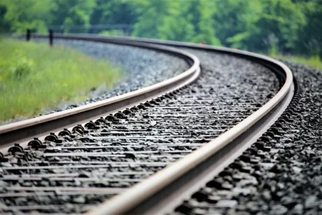 Șine de tren curbează printre vegetație, semn al unei rute feroviare.