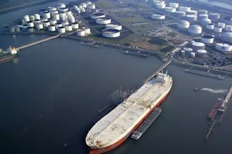 Vedere aeriană a unui supertanc petrolier în port, cu rezervoare în fundal.