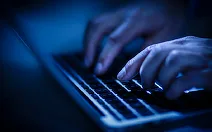 Mâini tastând pe un laptop în întuneric, simbolizând activități online.