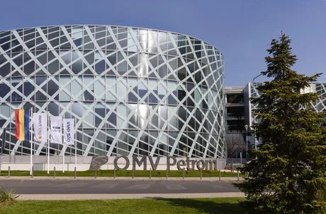 Clădire modernă OMV Petrom, cu fațadă din sticlă și arbori în jur.