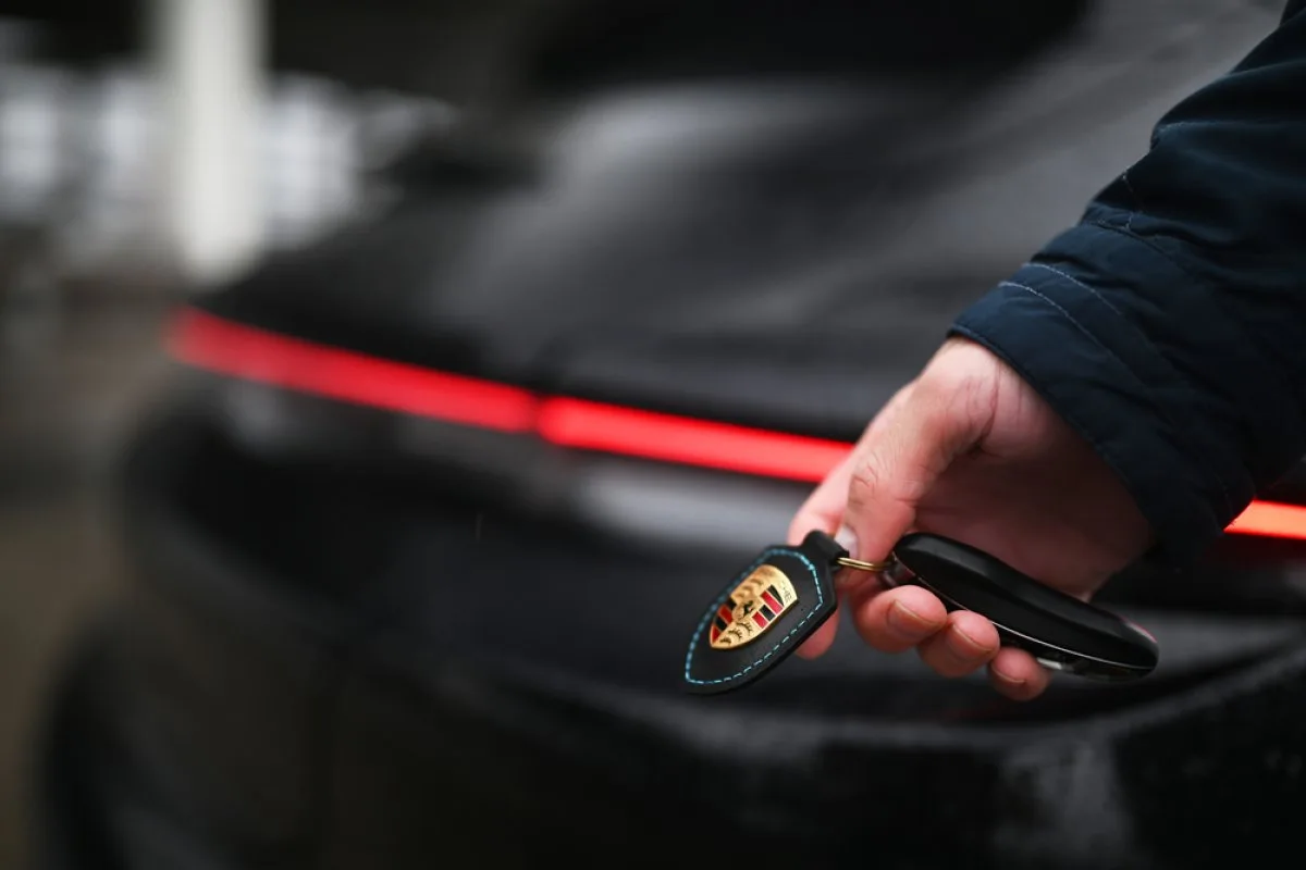 Cheie Porsche în mână, cu logo pe fundalul unei mașini electrice.