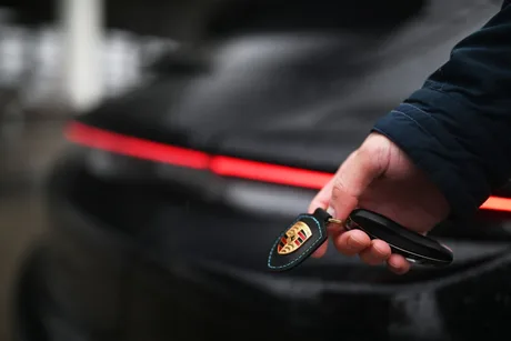 Cheie Porsche în mână, cu logo pe fundalul unei mașini electrice.