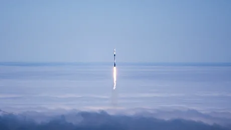 Rachetă lansată de SpaceX, traversând nori pe cerul albastru.