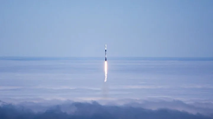 Rachetă lansată de SpaceX, traversând nori pe cerul albastru.