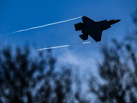 Avion de luptă zburând pe un fundal albastru, cu urme de condens în urma sa.
