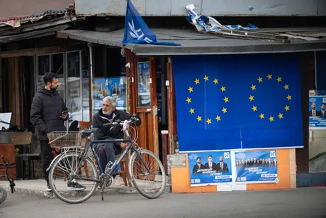 Oameni discutând lângă un magazin cu steagul Uniunii Europene expus.