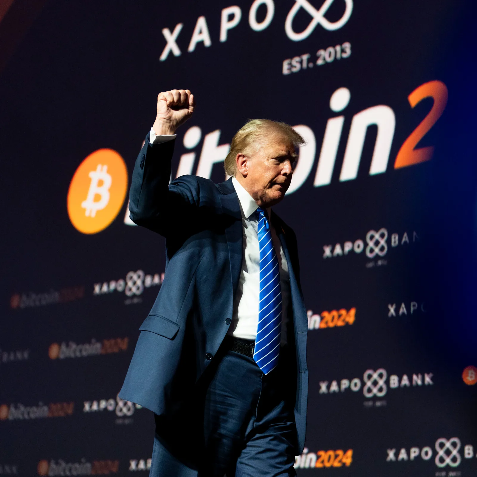Un bărbat îmbrăcat elegant ridică pumnul într-un eveniment legat de cripto.