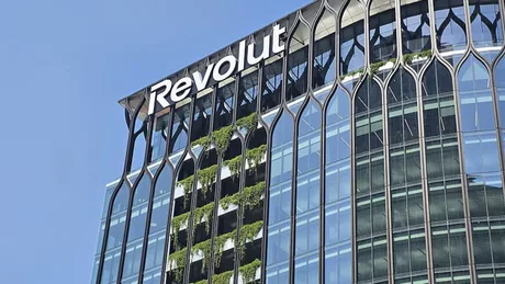 Clădire modernă cu logo-ul Revolut pe fațadă, sub un cer senin.