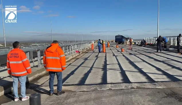 Lucrări de construcție pe un drum, cu muncitori în echipamente de siguranță.
