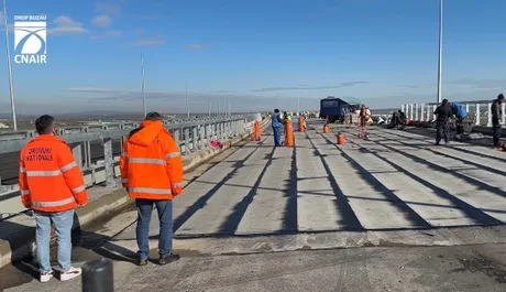 Lucrări de construcție pe un drum, cu muncitori în echipamente de siguranță.
