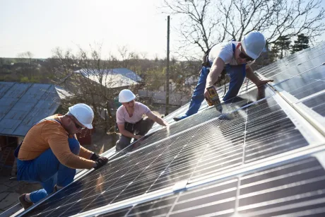 Muncitori instalând panouri solare pe acoperișuri, contribuind la modernizarea energiei.