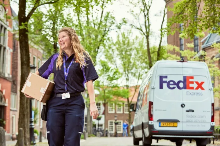 O angajată FedEx livrând un colet într-un mediu urban verde.