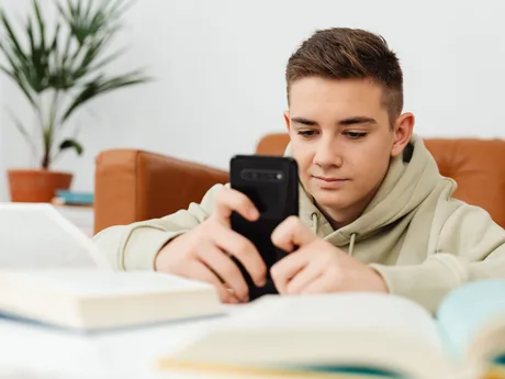 Tânăr utilizator interacționând cu telefonul mobil în timp ce studiază.