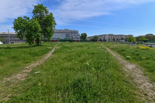 Teren verde cu iarbă, pregătit pentru dezvoltări imobiliare în oraș.
