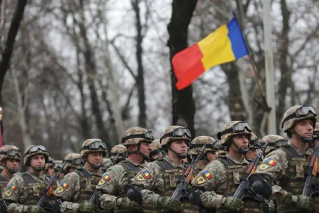 Soldați români în timpul unei parade militare, cu steagul național în fundal.