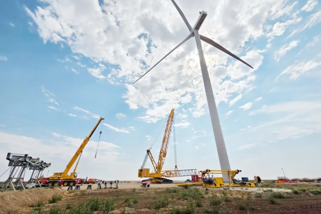 Turbine eoliene în construcție pe un câmp deschis, sub un cer senin.