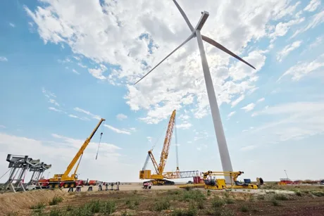 Turbine eoliene în construcție pe un câmp deschis, sub un cer senin.