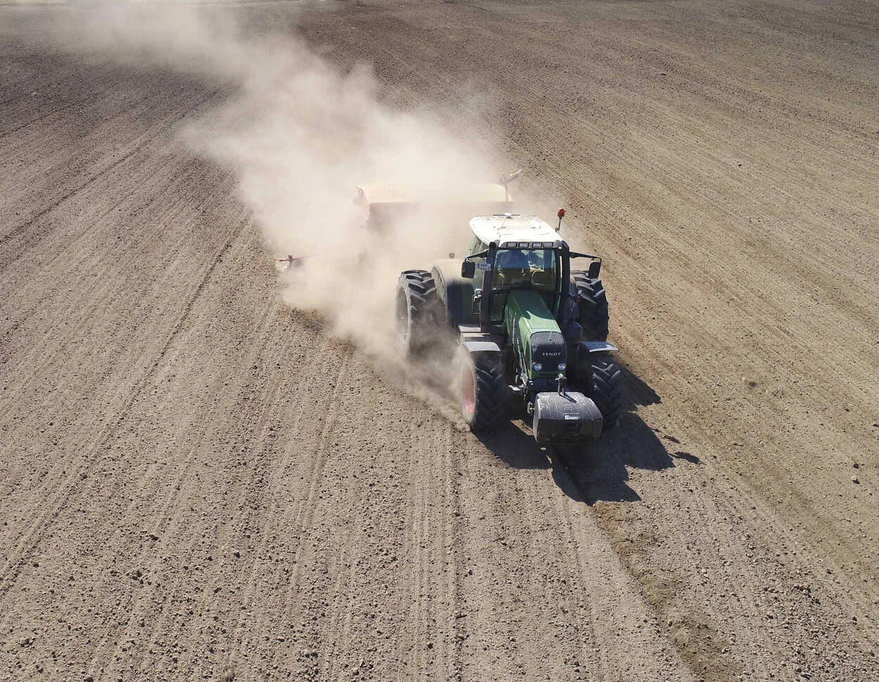 Tractor semănând rapiță pe un câmp uscat, în condiții de secetă.
