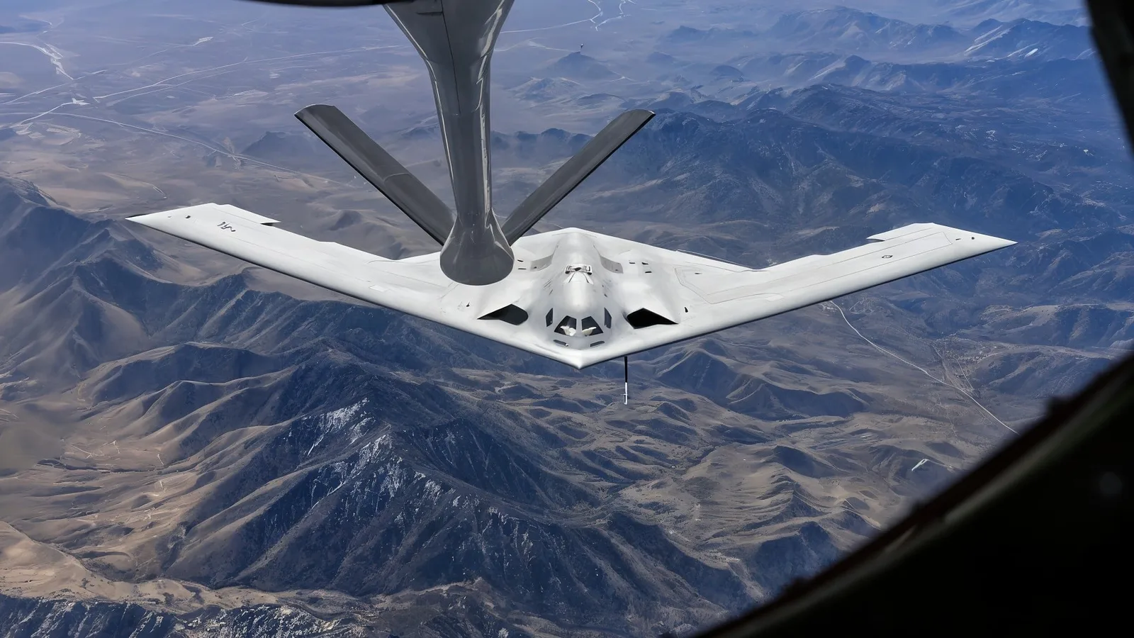 Bombardierul B-21 Raider în timpul realimentării aeriene, zburând deasupra peisajului montan.