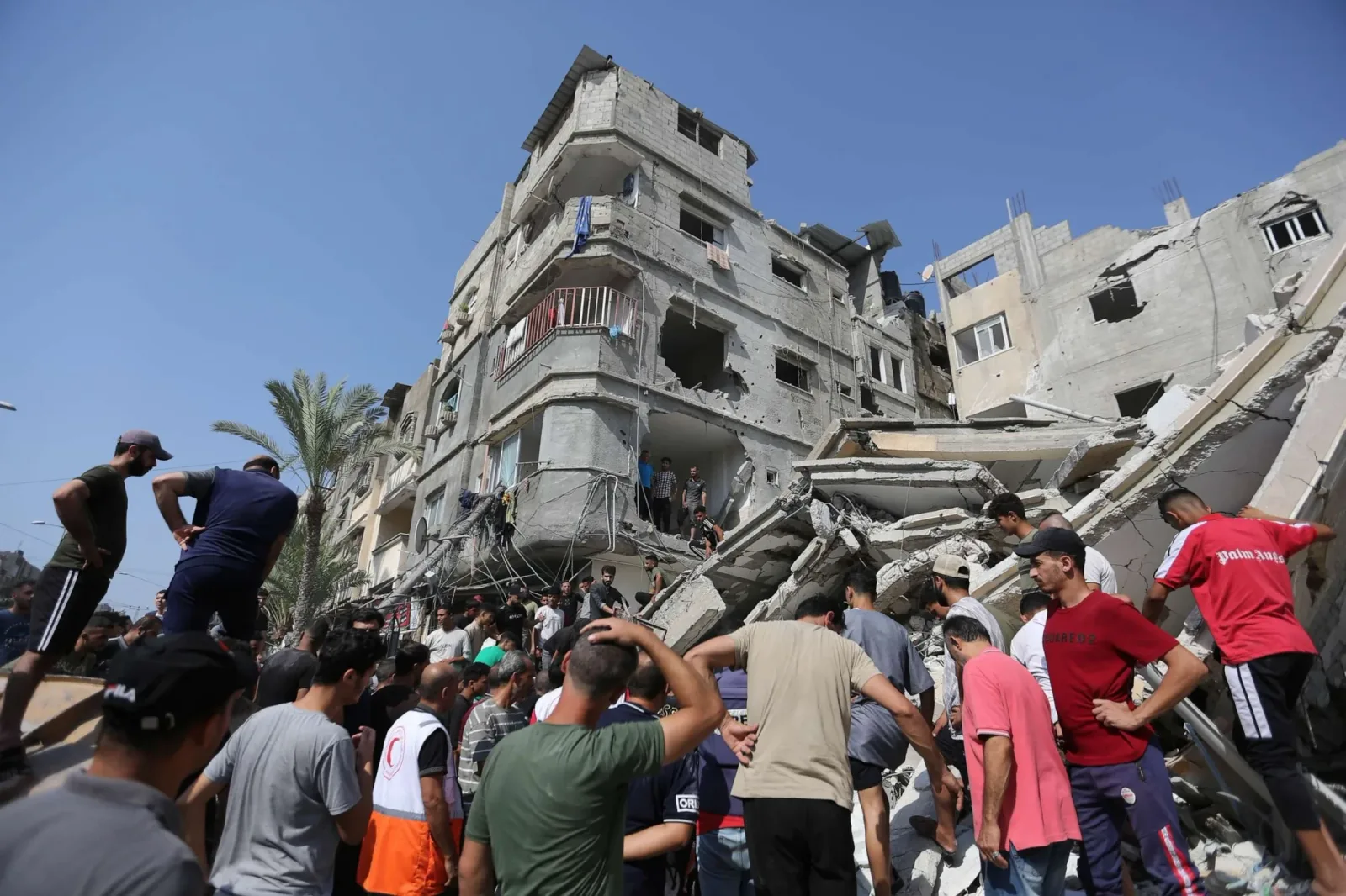 Oameni adunați în jurul unei clădiri distruse în Gaza.
