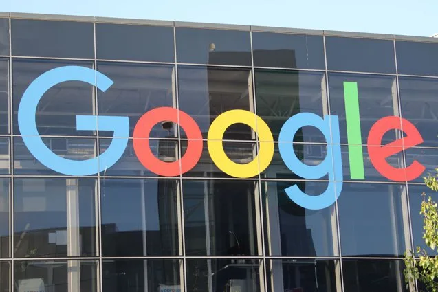 Logo-ul Google pe o clădire modernă, reflectând soarele.