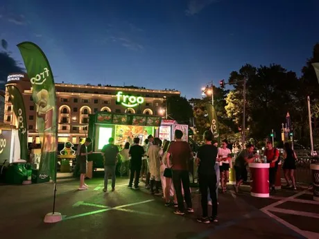 Oameni adunați la un eveniment Froo, cu lumini și bannere verzi în fundal.