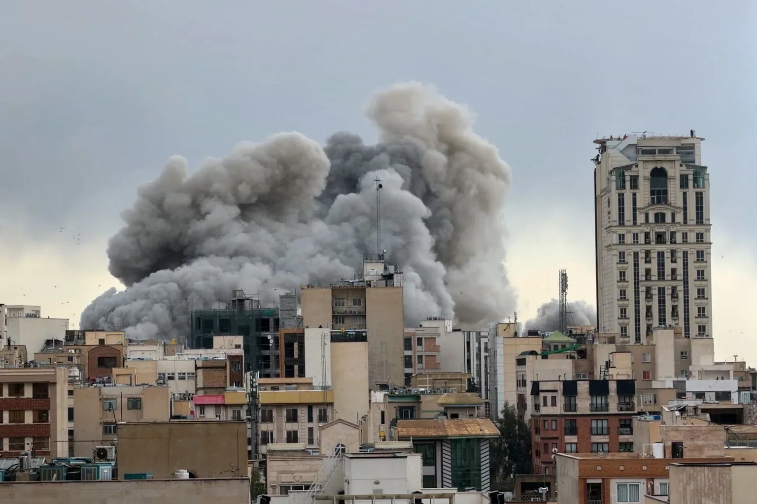 Fum gros se ridică deasupra clădirilor distruse în Iran.