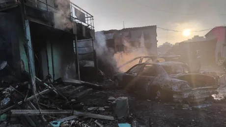Distrugeri cauzate de atacurile rusești în Ucraina, cu mașini avariate și fum.