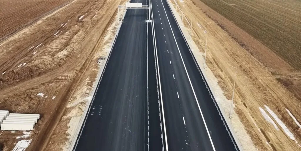 Vedere aeriană a unei autostrăzi în construcție, cu pământ arat pe margini.