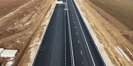 Vedere aeriană a unei autostrăzi în construcție, cu pământ arat pe margini.