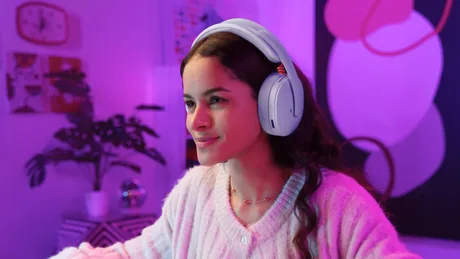 Tânără zâmbitoare purtând căști wireless Logitech G325 în mediu colorat