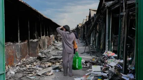 O femeie în fața unui market distrus, cu rafturi goale și moloz în jur.