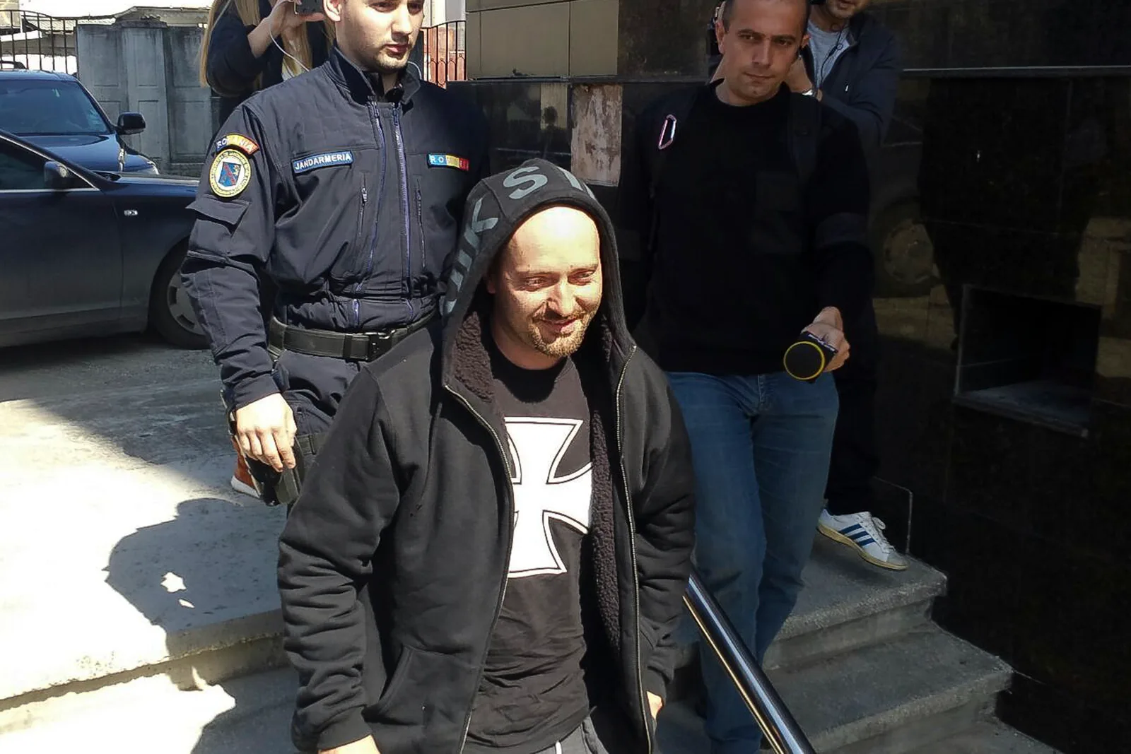 Rapperul Cheloo, escortat de polițiști, părăsește o clădire.