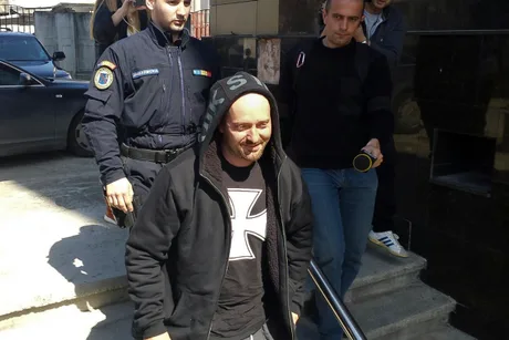 Rapperul Cheloo, escortat de polițiști, părăsește o clădire.