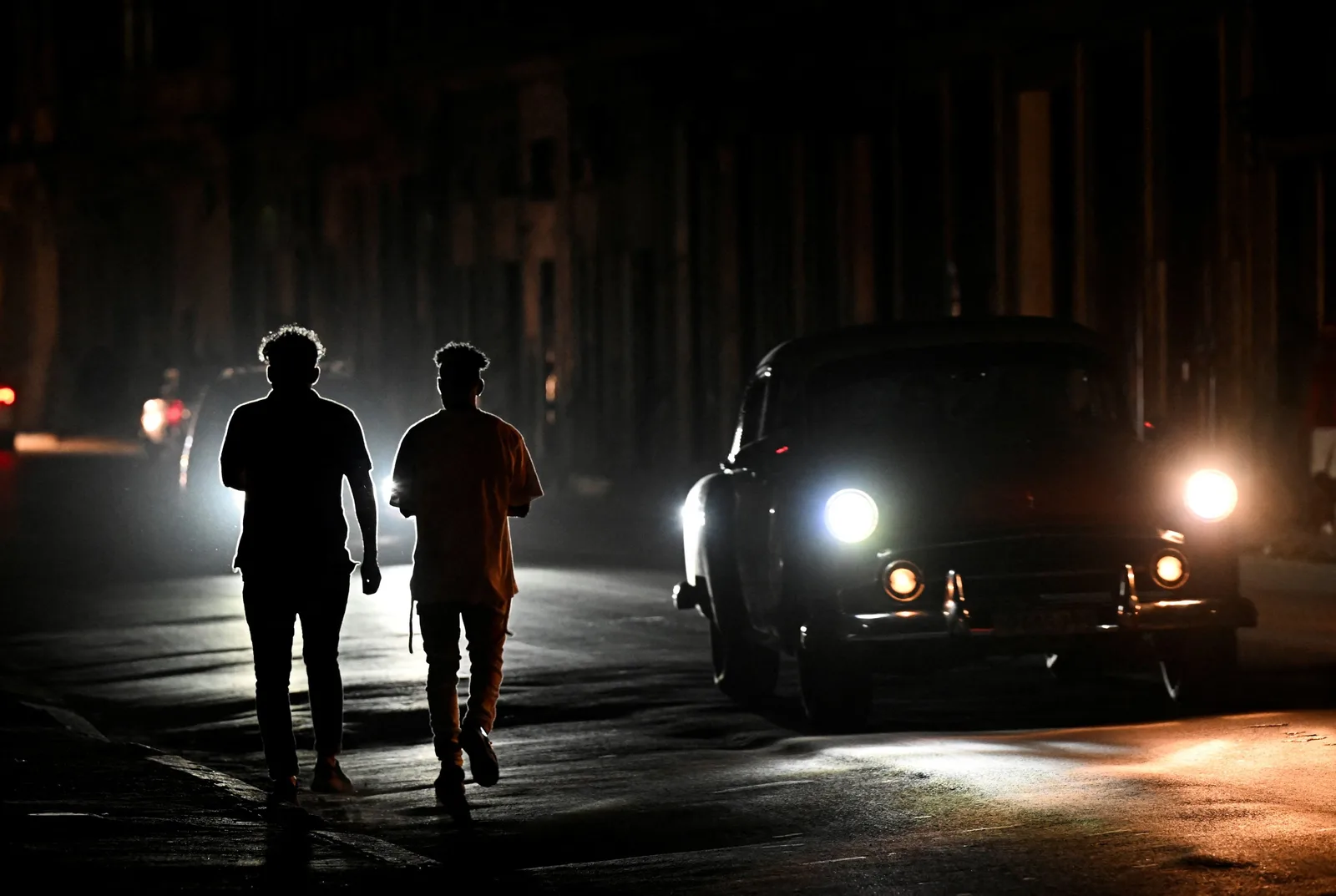 Două persoane merg pe o stradă întunecată, luminile orașului fiind slabe.