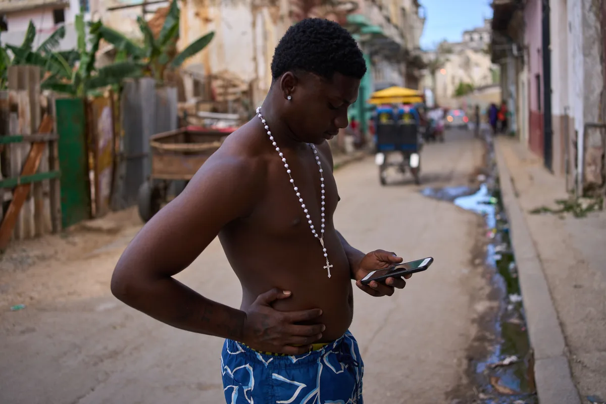 Tânăr pe stradă, verificând telefonul în timpul penelor de curent din Cuba.