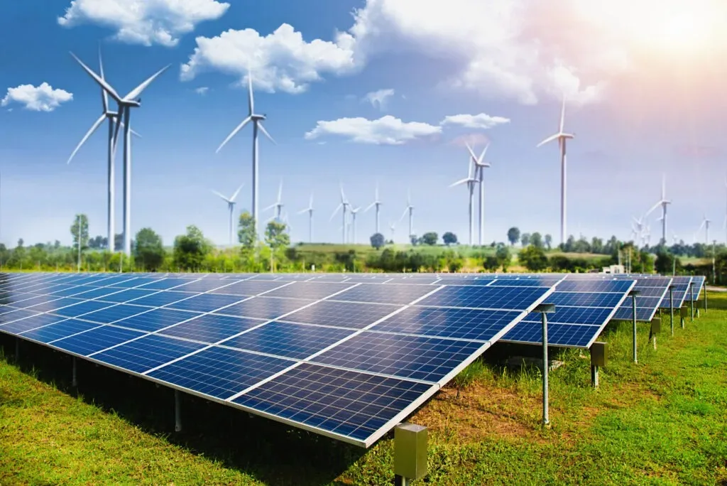 Parcuri fotovoltaice cu turbine eoliene pe un câmp verde, sub un cer senin.