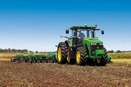 Tractor lucrând pe un câmp agricol în soare.