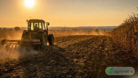 Tractor lucrând pe câmp în lumina apusului, în condiții de caniculă.