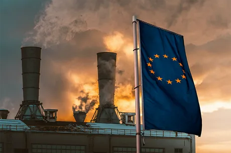 Steag european în fața unei fabrici cu emisii de fum.