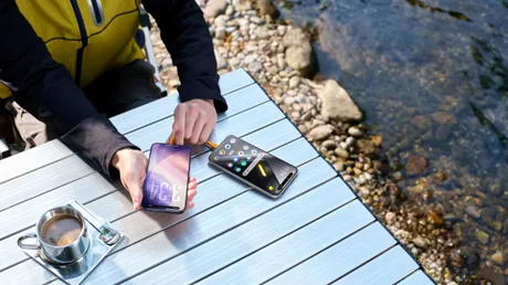 Utilizator interacționând cu smartphone-uri pe o masă lângă apă.